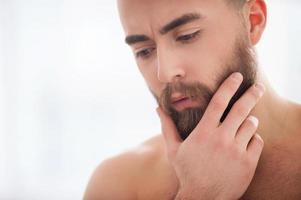 barba bonito. retrato de homem de barba jovem confiante segurando a mão no queixo e desviar o olhar foto