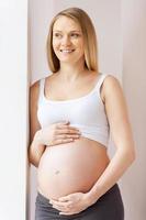 esperando um bebê. mulher grávida feliz encostada na parede e olhando para longe foto