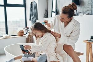 linda jovem mãe combinando o cabelo da filha enquanto fazia a rotina matinal foto