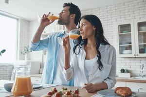 jovem casal bebendo suco de laranja enquanto passa o tempo na cozinha doméstica foto