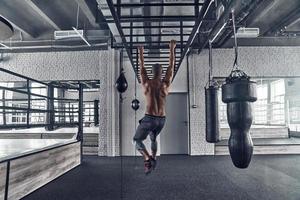 rumo ao estilo de vida mais saudável. vista traseira de comprimento total do jovem africano sem camisa fazendo flexões durante o exercício no ginásio foto