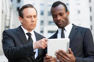 consultoria com especialista. dois homens de negócios confiantes olhando para o tablet digital enquanto um deles apontando com o dedo foto