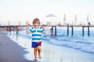 garotinho feliz correndo na praia foto