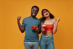 lindo jovem casal africano sorrindo e gesticulando em pé contra um fundo amarelo foto