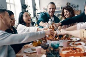 amigos próximos. grupo de jovens em roupas casuais, brindando e sorrindo enquanto fazia um jantar dentro de casa foto