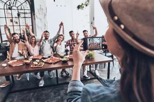 ficando loucos juntos. jovem fotografando um grupo de amigos usando telefone inteligente enquanto eles fazem um jantar foto