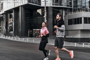 sério sobre ficar em forma. comprimento total do jovem casal em roupas esportivas correndo pela rua da cidade juntos foto