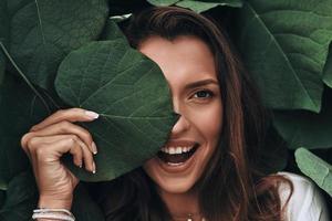 beleza natural. mulher jovem e atraente olhando para a câmera e sorrindo em pé entre as folhas ao ar livre foto