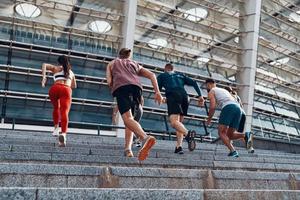 vista traseira de corpo inteiro de jovens em roupas esportivas correndo durante o exercício nas escadas ao ar livre foto