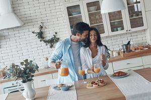 casal jovem feliz preparando o café da manhã juntos e sorrindo enquanto passa o tempo na cozinha doméstica foto
