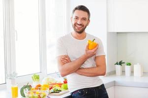 alimentação saudável é vida saudável. jovem bonito segurando pimenta amarela fresca e sorrindo em pé na cozinha foto