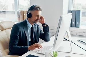 empresário concentrado em fones de ouvido tendo conferência na web enquanto está sentado em seu local de trabalho foto