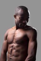 viril e musculoso. homem africano sem camisa posando em pé contra um fundo cinza foto