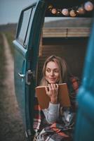 inspirada em seu livro... jovem atraente coberta com cobertor olhando para longe e sorrindo enquanto está sentado dentro da mini van azul estilo retrô foto