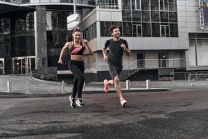 lado a lado pela cidade. comprimento total do jovem casal em roupas esportivas correndo pela rua da cidade juntos foto