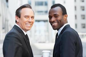 o melhor do mundo dos negócios. dois homens de negócios confiantes olhando por cima do ombro e sorrindo em pé ao ar livre foto