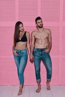 parecendo incrível. comprimento total do lindo casal jovem de mãos dadas em pé contra um fundo rosa foto