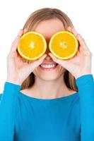 óculos laranja. jovem brincalhão segurando pedaços de laranja na frente dos olhos e sorrindo enquanto isolado no branco foto