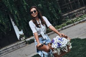 roda despreocupada. mulher jovem e atraente em roupas casuais sorrindo enquanto anda de bicicleta ao ar livre foto