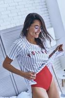 mostrando seu corpo incrível. bela jovem mantendo os olhos fechados e sorrindo em pé no quarto foto