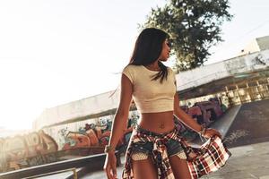 beleza real. mulher jovem e atraente ajustando a camisa em pé no parque de skate ao ar livre foto