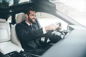 no caminho do sucesso. confiante jovem empresário sentado no banco da frente e sorrindo enquanto dirige um carro foto