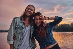 casal brincalhão. casal jovem feliz em roupas casuais sorrindo e olhando para a câmera em pé perto do lago foto