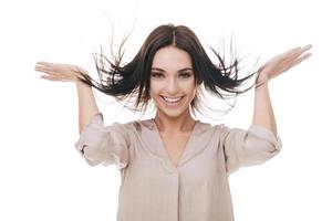 eu amo meu cabelo. mulher jovem e atraente tocando seu cabelo e sorrindo em pé contra um fundo branco foto