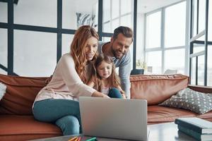 jovem família linda com garotinha se unindo e sorrindo enquanto estiver usando o laptop em casa foto