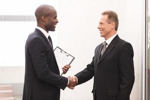 reunião de negócios. dois homens de negócios alegres apertando as mãos e olhando um ao outro foto