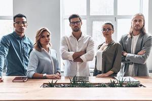 confiante e inteligente. grupo de jovens modernos em roupas casuais inteligentes, olhando para a câmera em pé no escritório criativo foto