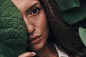 verdadeira beleza. mulher jovem e atraente olhando para a câmera em pé entre as folhas ao ar livre foto