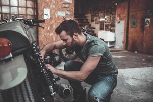 ele sabe tudo sobre motos. jovem confiante reparando moto perto de sua garagem foto