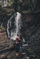 melhor viagem. vista traseira de corpo inteiro do jovem casal abraçando em pé perto da cachoeira foto