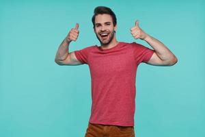 bonito jovem sorridente em roupas casuais, olhando para a câmera e mostrando os polegares para cima foto