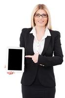 apresentando seu novo tablet. bela empresária madura segurando o tablet digital e apontando-o em pé isolado no branco foto