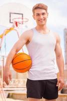 jogador de basquete. bonito jovem jogador de basquete masculino em pé ao ar livre e sorrindo foto