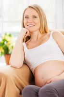 mulher grávida sonhando. mulher grávida feliz sentada na cadeira e segurando a mão no queixo foto