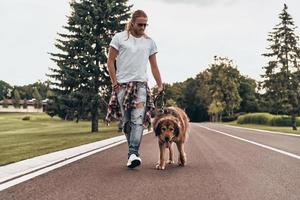 curtindo uma boa caminhada. comprimento total de jovem bonito andando com seu cachorro enquanto passa o tempo ao ar livre foto