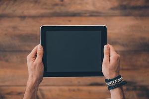 tablet que facilita a vida. vista superior do homem segurando o tablet digital em pé no chão de madeira foto