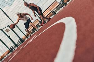 jogar basquete. dois jovens em roupas esportivas jogando basquete enquanto passam tempo ao ar livre foto