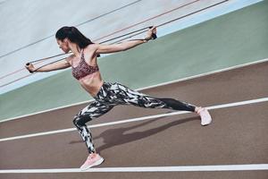 nunca desista. mulher jovem e bonita em roupas esportivas exercitando usando banda de resistência em pé na pista de corrida ao ar livre foto