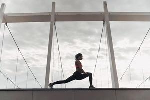 exercícios de relaxamento. mulher jovem e moderna em roupas esportivas, alongamento enquanto se aquece ao ar livre foto