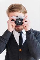 focando em você. homem jovem barba focando em você com sua câmera retro em pé contra um fundo cinza foto