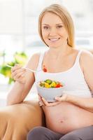 mulher grávida comendo salada. mulher grávida feliz sentada na cadeira e comendo salada foto