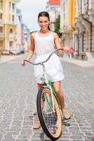 garota da cidade. comprimento total da bela jovem sorridente andando de bicicleta ao longo da rua foto