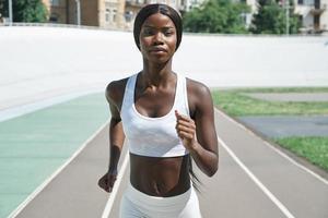 bela jovem africana em roupas esportivas correndo na pista ao ar livre foto