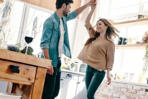 momentos felizes juntos. comprimento total do lindo casal jovem em roupas casuais dançando e sorrindo em pé na cozinha em casa foto