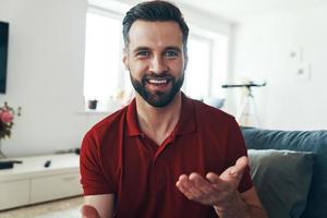 jovem bonito em roupas casuais, olhando para a câmera e sorrindo enquanto passa o tempo dentro de casa foto