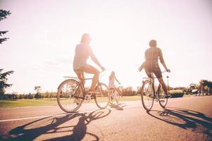 aproveitando o tempo despreocupado juntos. vista traseira de jovens alegres andando de bicicleta ao longo de uma estrada juntos foto